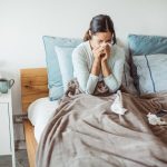 Woman sitting up in bed and blowing her nose to clear congestion on one side