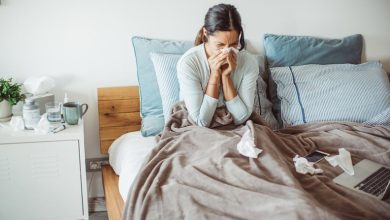 Woman sitting up in bed and blowing her nose to clear congestion on one side