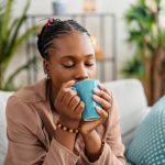 Woman sitting on the sofa in the living room, drinking protein coffee.