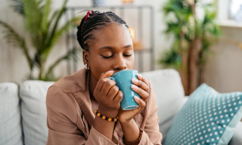 Woman sitting on the sofa in the living room, drinking protein coffee.