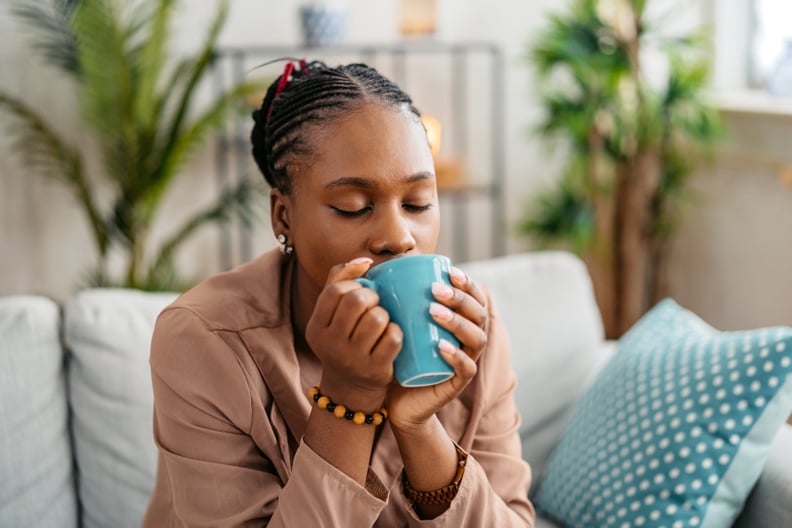 Woman sitting on the sofa in the living room, drinking protein coffee.