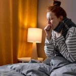 Woman sitting in bed, coughing at night.