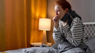 Woman sitting in bed, coughing at night.