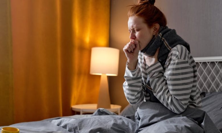 Woman sitting in bed, coughing at night.