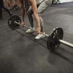 Female cross training ter using a barbell to prefrom a deadlift while at a gym.