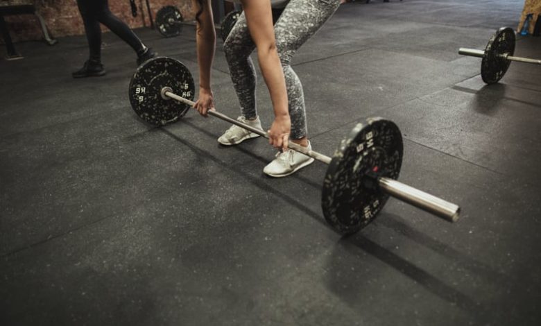 Female cross training ter using a barbell to prefrom a deadlift while at a gym.