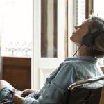 Woman sitting in a chair while wearing headphones and listening to music with eyes closed.