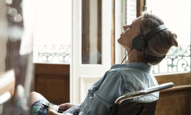 Woman sitting in a chair while wearing headphones and listening to music with eyes closed.