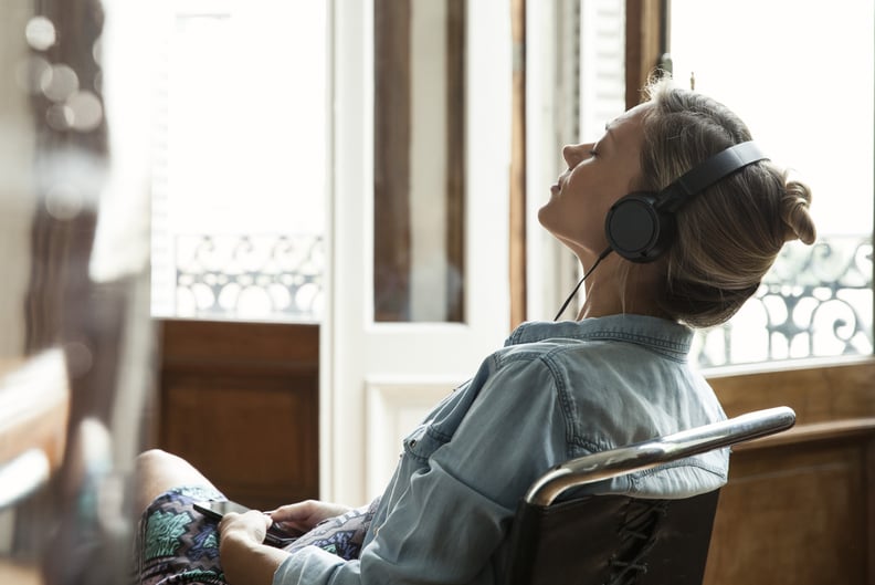 Woman sitting in a chair while wearing headphones and listening to music with eyes closed.