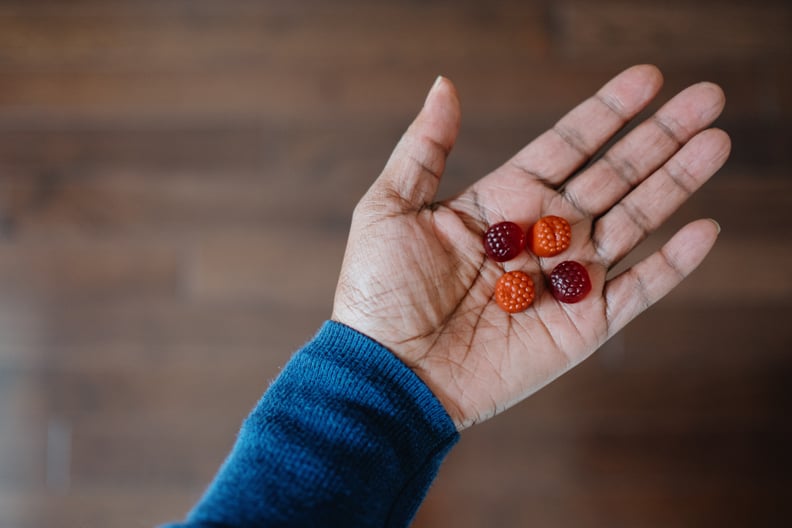 Close-up of unrecognizable woman holding four melatonin gummy supplements in the palm of her hand.