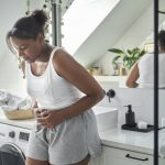 Young African-American woman standing in the bathroom and feeling pain in the stomach.