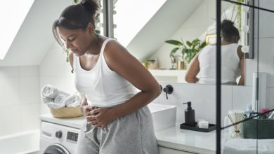 Young African-American woman standing in the bathroom and feeling pain in the stomach.