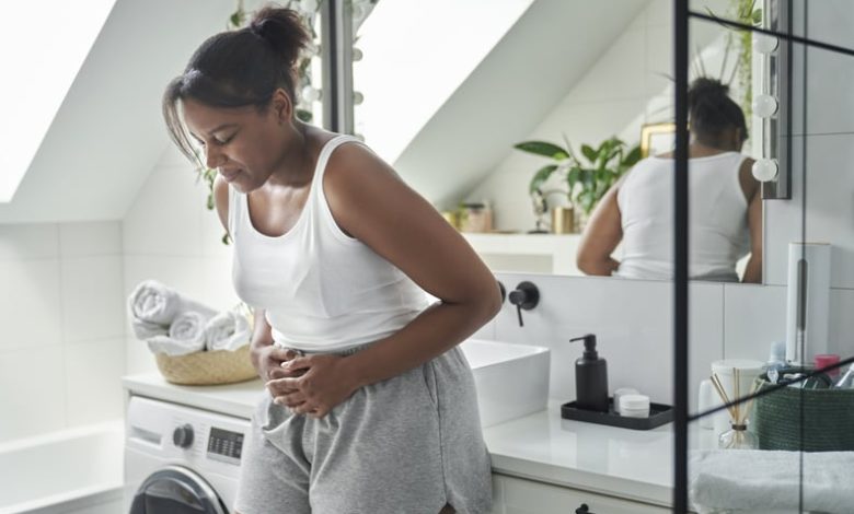 Young African-American woman standing in the bathroom and feeling pain in the stomach.