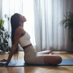 Side view of young woman sitting on blue yoga mat ready for a somatic training session