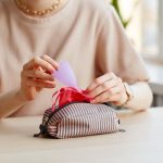 Woman putting menstrual cup in cosmetic bag with other essentials.