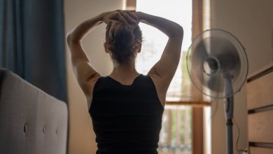 A young woman with her hands behind her head in front of a fan.