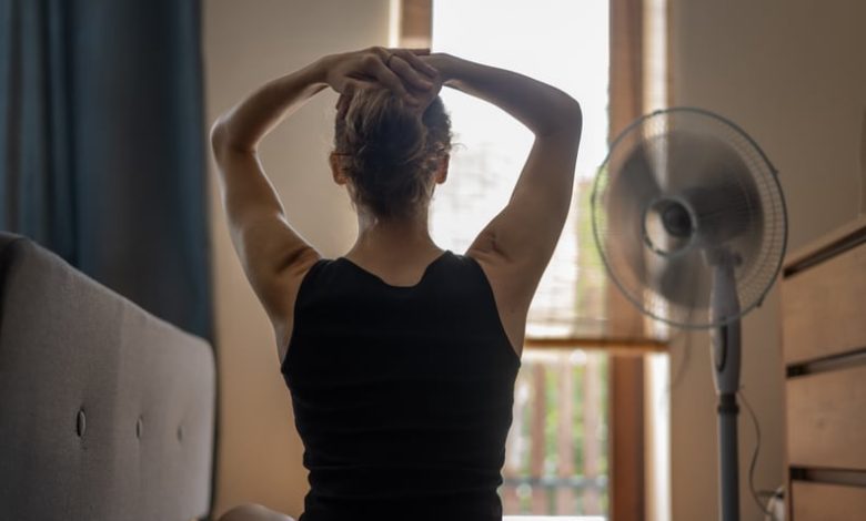 A young woman with her hands behind her head in front of a fan.