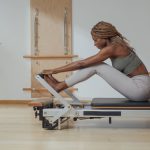 Beautiful African smiling sportswoman doing pilates exercise on reformer as part of the 3-2-1 workout method