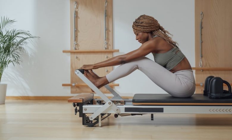 Beautiful African smiling sportswoman doing pilates exercise on reformer as part of the 3-2-1 workout method