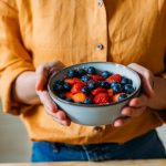 Close-up of a person holding a bowl filled with fresh strawberries and blueberries.