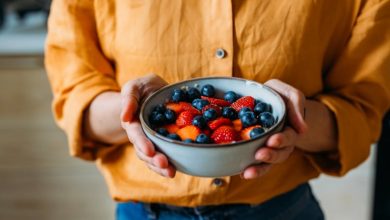 Close-up of a person holding a bowl filled with fresh strawberries and blueberries.