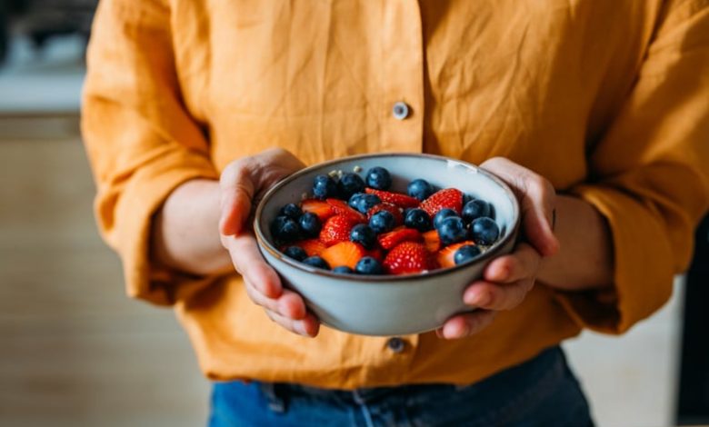 Close-up of a person holding a bowl filled with fresh strawberries and blueberries.