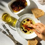 A woman dips a torn piece of hand made artisan bread in extra virgin olive oil on table top shot.