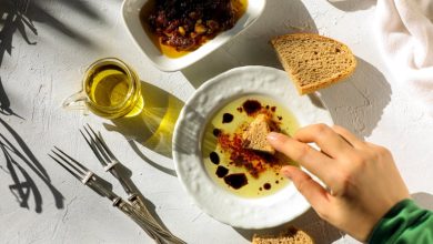 A woman dips a torn piece of hand made artisan bread in extra virgin olive oil on table top shot.