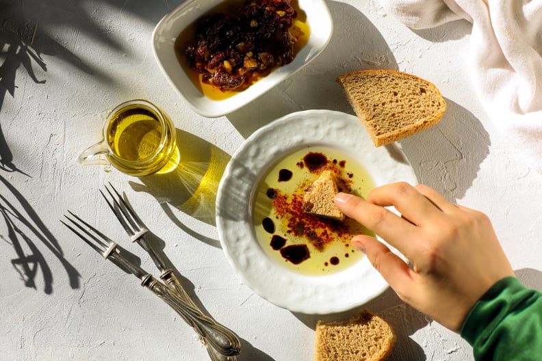 A woman dips a torn piece of hand made artisan bread in extra virgin olive oil on table top shot.