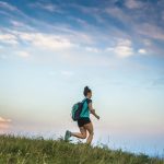 Young woman running in the mountains with backpack on her shoulders.