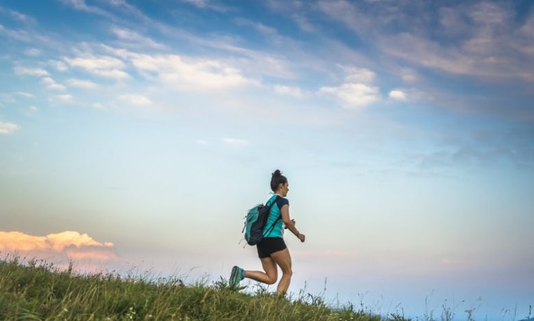 Young woman running in the mountains with backpack on her shoulders.