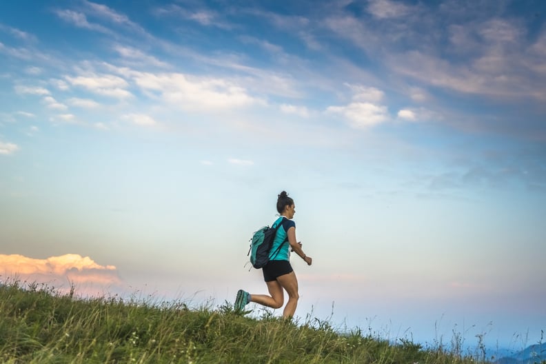 Young woman running in the mountains with backpack on her shoulders.