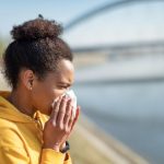 Black woman in yellow hoodie sneezing.