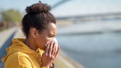 Black woman in yellow hoodie sneezing.