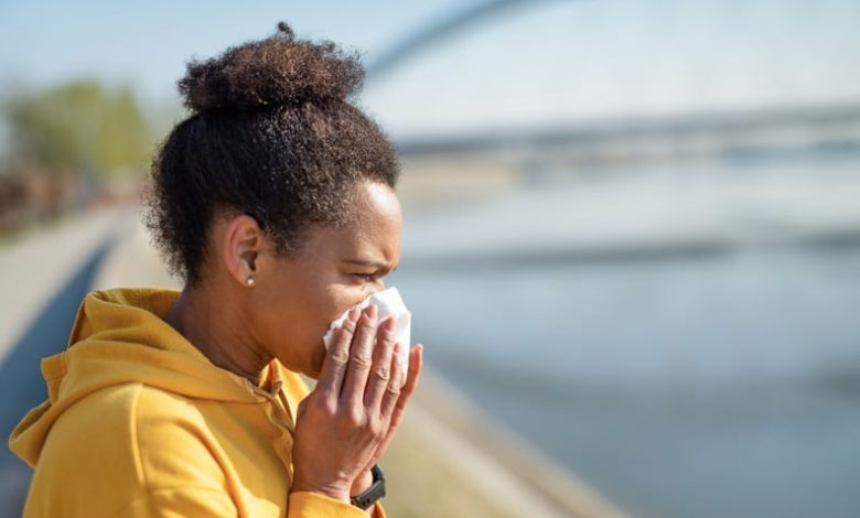 Black woman in yellow hoodie sneezing.