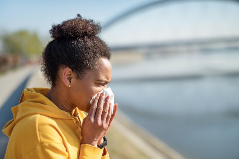 Black woman in yellow hoodie sneezing.