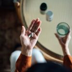 Woman taking medicine in hand with a glass of water, chronic illness during the holidays.