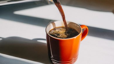 Coffee being poured into an orange mug on a white countertop.