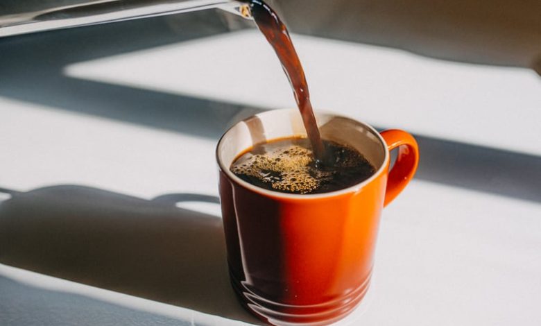 Coffee being poured into an orange mug on a white countertop.